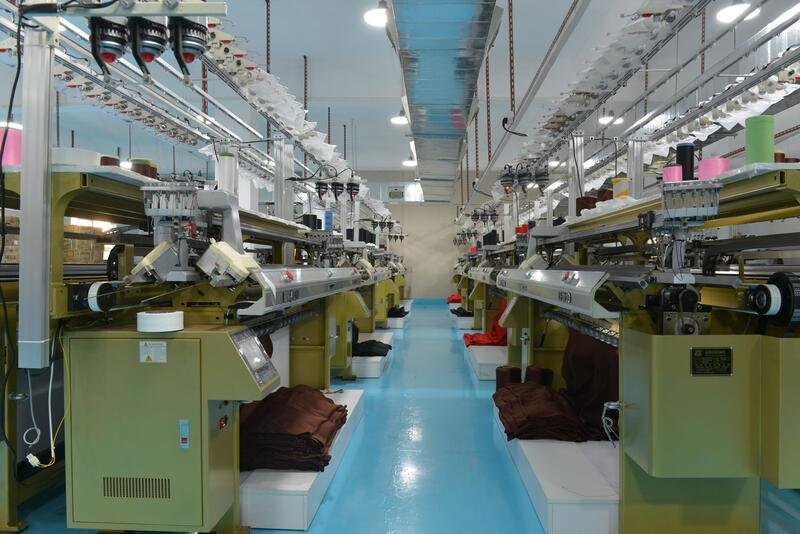 Industrial weaving workshop for bandage dress fabric, featuring multiple knitting machines and colorful spools of yarn.